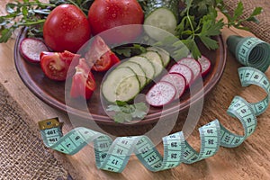 Vegetables in a ceramic plate on an uncouth board. Measuring tape. Low calorie diet concept