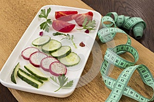 Vegetables in a ceramic plate on an uncouth board. Measuring tape. Low calorie diet concept