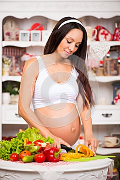 Vegetables and diet during pregnancy. Beautiful pregnant woman in the kitchen preparing a meal