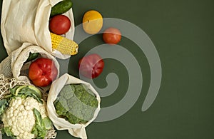 Vegetables in eco bag on green surface with a copy space. Pepper, tomato, corn, cucumber, broccoli, cauliflower in