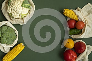 Vegetables in eco bag on green surface with a copy space. Pepper, tomato, corn, cucumber, broccoli, cauliflower in