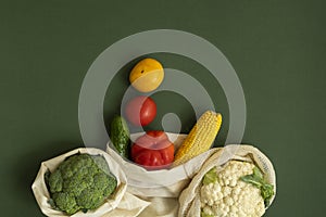 Vegetables in eco bag on green surface with a copy space. Pepper, tomato, corn, cucumber, broccoli, cauliflower in