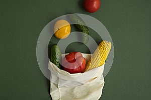 Vegetables in eco bag on green surface. Pepper, tomato, corn, cucumber, broccoli, cauliflower in reusable shopping eco