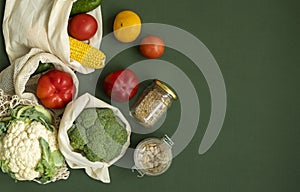 Vegetables in eco bag and nuts in a glass jar on green surface. Pepper, tomato, corn, cucumber, broccoli, cauliflower in