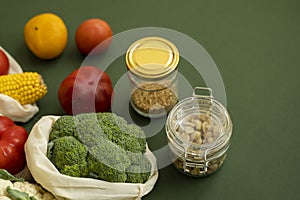 Vegetables in eco bag and nuts in a glass jar on green surface. Pepper, tomato, corn, cucumber, broccoli, cauliflower in