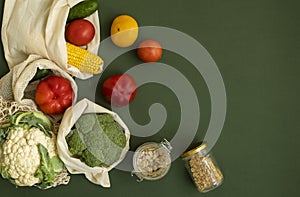 Vegetables in eco bag and nuts in a glass jar on green surface. Pepper, tomato, corn, cucumber, broccoli, cauliflower in