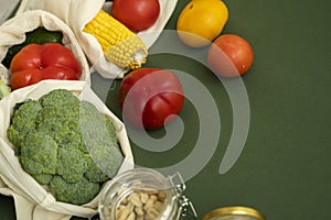 Vegetables in eco bag and nuts in a glass jar on green surface. Pepper, tomato, corn, cucumber, broccoli, cauliflower in