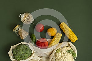 Vegetables in eco bag and nuts in a glass jar on green surface. Pepper, tomato, corn, cucumber, broccoli, cauliflower in