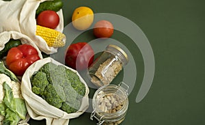 Vegetables in eco bag and nuts in a glass jar on green surface. Pepper, tomato, corn, cucumber, broccoli, cauliflower in