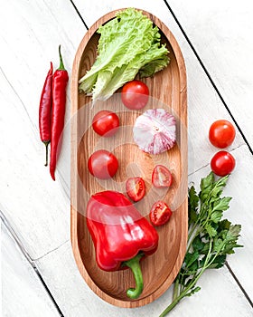 Vegetables, fresh salad and cherry tomatoes, parsley, bell red pepper, garlic on wooden cutting board.