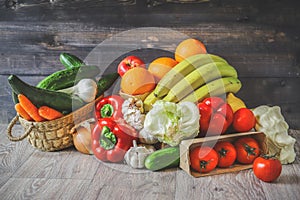 Vegetables and fruits on a graphite wooden background: in a box are tomatoes, cucumber, garlic, large red peppers, Iceberg lettuce