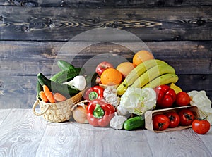 Vegetables and fruits on a graphite wooden background: in a box are tomatoes, cucumber, garlic, large red peppers, Iceberg lettuce