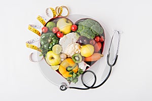 vegetables and fruits laying in heart shaped dish near stethoscope and measuring tape