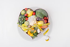 vegetables and fruits laying in heart shaped dish near stethoscope and measuring tape