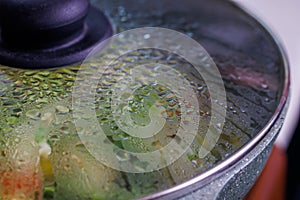 vegetables in frying pan covered with glass lid with water condensation drops on inner surface