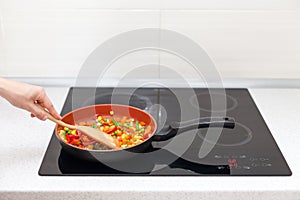 Vegetables are in a frying pan. Woman cooking colourful fresh vegetables on an electric stove.