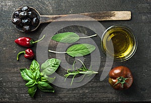 Vegetables and herbs on dark rustic wooden background. Greek black olives, fresh green sage, rosemary, basil herbs, oil