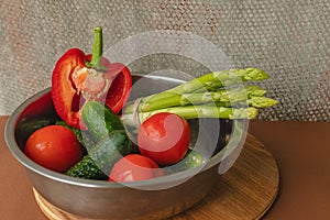 Vegetables lie in a metal bowl: tomatoes, asparagus, cucumbers, red bell peppers . on a wooden board and brown