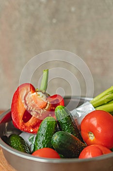 Vegetables lie in a metal bowl: tomatoes, asparagus, cucumbers, red bell peppers . on a wooden board and brown