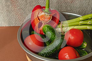 Vegetables lie in a metal bowl: tomatoes, asparagus, cucumbers, red bell peppers . on a wooden board and brown