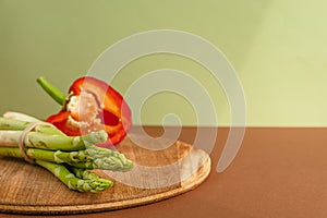 Vegetables lie on a wooden board: asparagus, red bell peppers. brown, light green background. place for text.