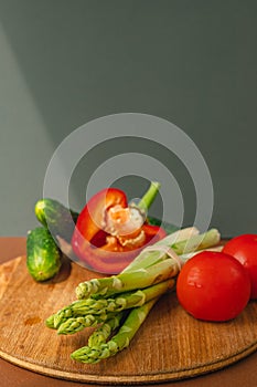 Vegetables lie on a wooden board: tomatoes, asparagus, cucumbers, red bell peppers. brown, dark gray background. place