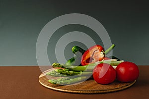 Vegetables lie on a wooden board: tomatoes, asparagus, cucumbers, red bell peppers. brown, dark gray background. place