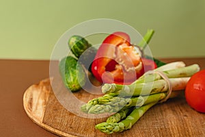 Vegetables lie on a wooden board: tomatoes, asparagus, cucumbers, red bell peppers. brown, light green background. place