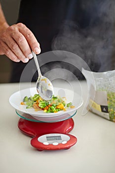 Vegetables are a must with every meal. Cropped image of a man spooning cooked vegetables onto a kitchen scale.