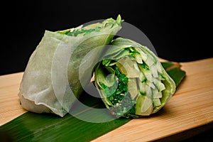 Vegetables rolls on a green leaf on a wood stand on a black background