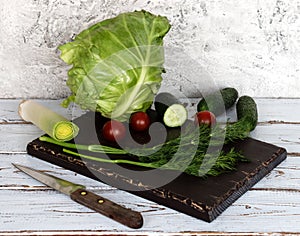 Vegetables for salad on a white rustic table, knife and old wooden board