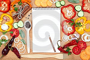 Vegetables, spices and notepad for recipes, on wooden table photo