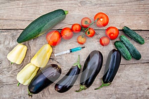 Vegetables and syringe with blue liquid on wooden background. Concept of Non-natural Products, Gmo