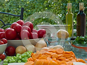 Vegetables, tomatoes, onions, chopped celery, carrot and basil leaves on the table with bottles of olive oil and balsamico vinegar