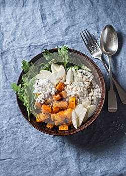 Vegetarian autumn pumpkin, barley, apples, arugula buddha bowl on a blue background