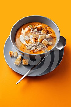 Vegetarian autumn pumpkin and carrot soup with cream, seeds and toasts on orange backgroumd.