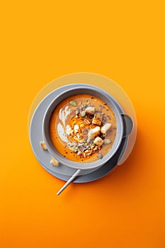 Vegetarian autumn pumpkin and carrot soup with cream, seeds and toasts on orange backgroumd.