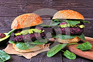 Vegetarian beet burgers with avocado and spinach against dark wood