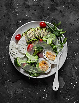 Vegetarian breakfast, snack bowl - salad mixed vegetables, boiled egg, grilled zucchini, cheese on a  dark background, top  view