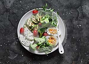 Vegetarian breakfast, snack bowl - salad mixed vegetables, boiled egg, grilled zucchini, cheese on a  dark background, top  view