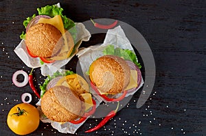 Vegetarian burgers with falafel, salad, cheese decorated with chili peppers, onion rings and yellow tomato on the black background