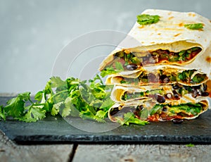 Vegetarian burritos wraps with beans, avocado and cheese on a slate