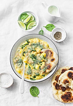 Vegetarian chickpea, spinach, potato curry plate and naan flatbread on white background, top view.