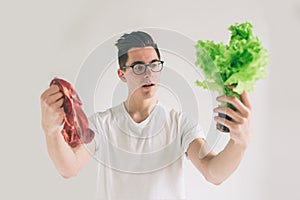 Vegetarian concept. Man offering a choice of meat or vegetables Salad leaves . Nerd is wearing glasses.