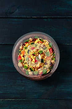 Vegetarian couscous salad with vegetables and herbs, overhead shot on a dark blue wooden background