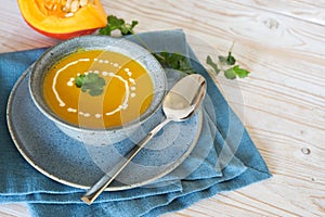 Vegetarian cream soup from red kuri squash with coriander herb garnish in a blue bowl on a light wooden table, copy space,