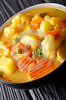 Vegetarian curry from potatoes, carrots, cauliflower, peas, tomatoes close-up in a bowl. vertical