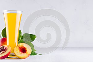 Vegetarian dieting drink - ripe fresh nectarines, green leaves and juice in elegant glass on white modern kitchen wood table.