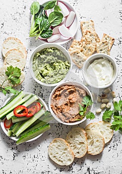Vegetarian dip table. Eggplant, harissa, walnuts dip, broccoli dip, soft tofu and fresh vegetables on a light background, top view photo