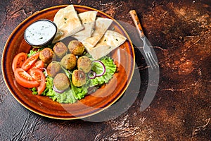 Vegetarian falafel with pita bread, fresh vegetables and sauce on a plate. Dark background. Top view. Copy space